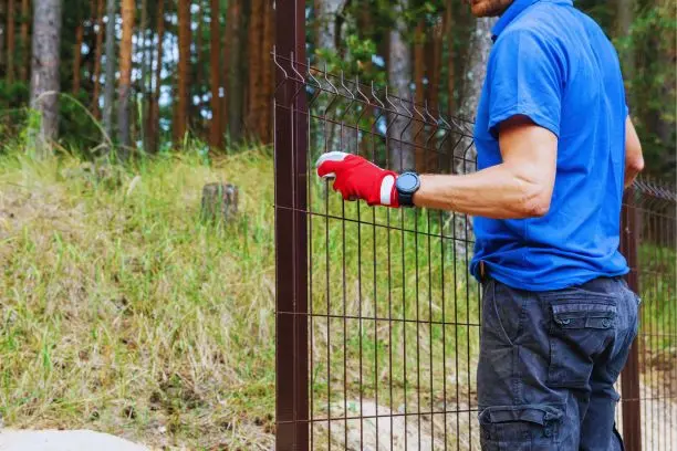 General contractors Sims NC 3 Worker installing a metal fence at the edge of woods
