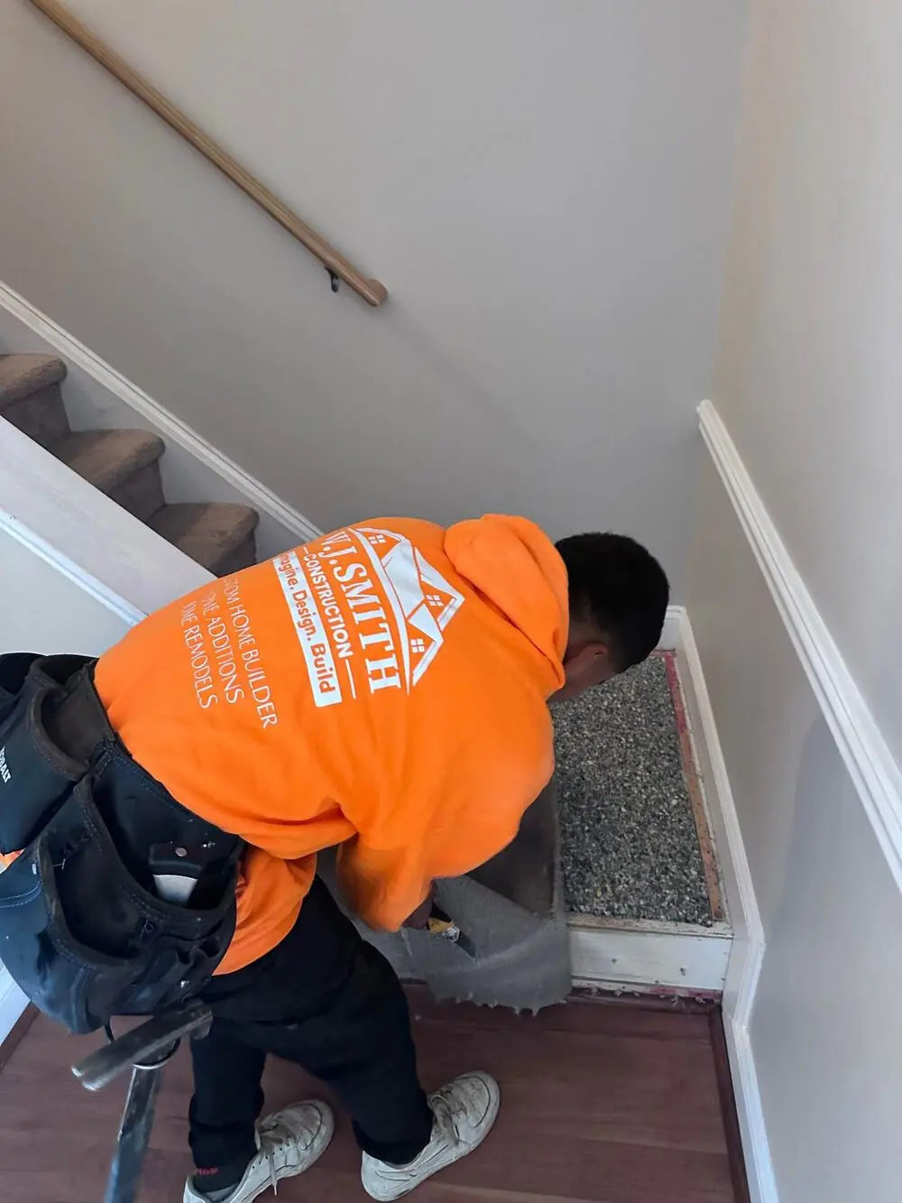 Home 18 Contractor in an orange W.J. Smith shirt working on interior stairs
